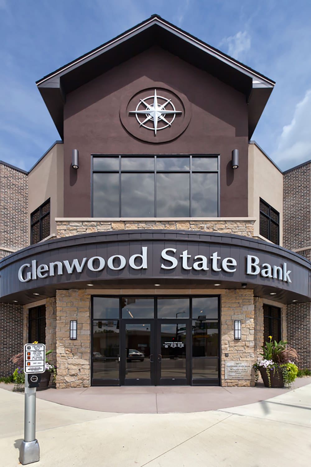 Front view of Glenwood State Bank building in Glenwood with a large compass decoration above the entrance, stone accents, and glass double doors, captured on a sunny day.